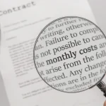 A person carefully reading a real estate contract with a magnifying glass.